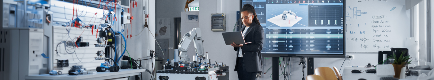 Automation Engineer Holding Laptop and Moving Bionic Arm With Written Code at Futuristic Factory